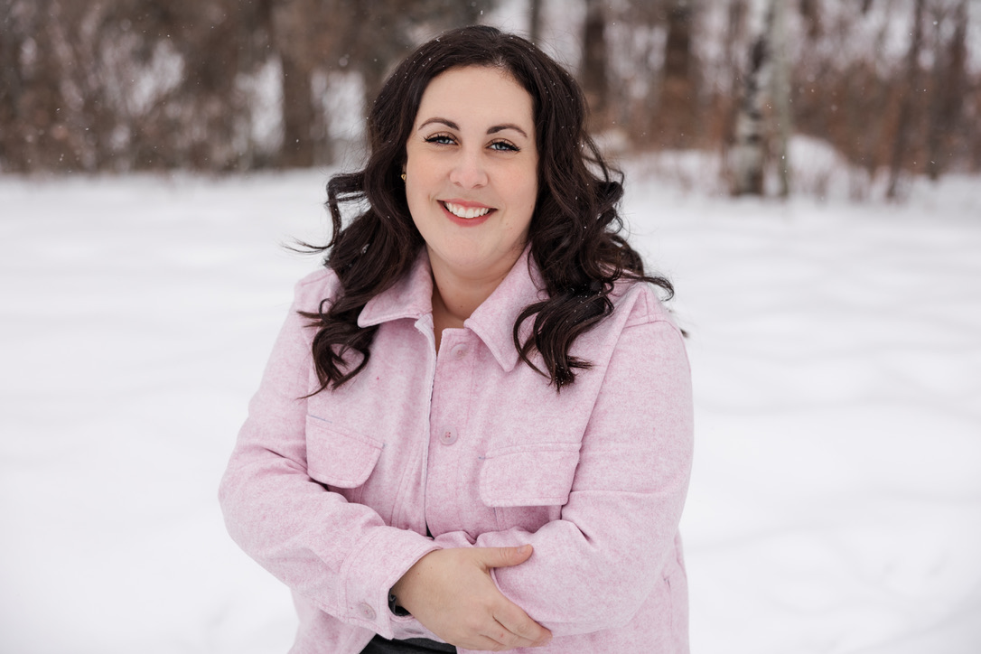 Woman with dark brown hair, light pink coat, stands outside on a snowy day.